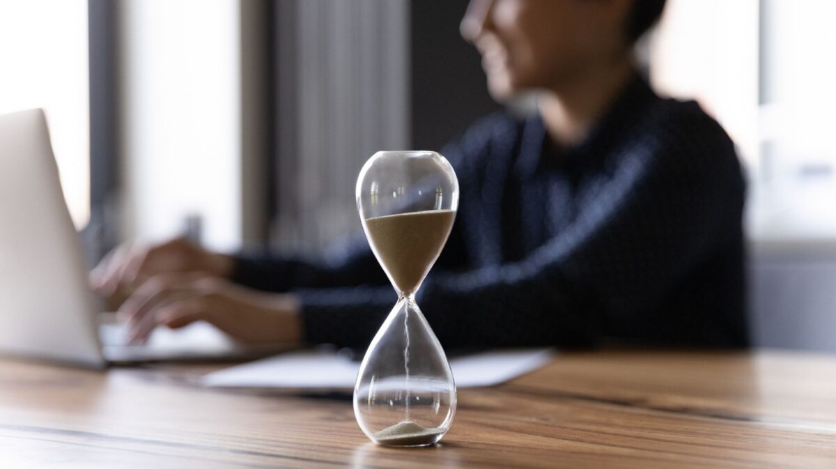 Hourglass on a desk with a business professional working on a laptop in the background